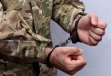 Person in military uniform handcuffed hands close up