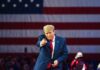 Donald Trump in front of American flag pointing toward camera.