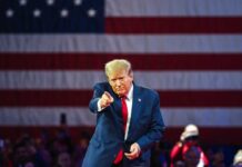 Donald Trump in front of American flag pointing toward camera.