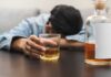 Person asleep at table holding drink glass