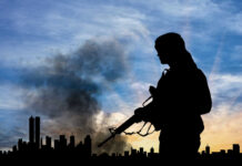 Terror, terrorist, terrorism, Silhouette of armed person with city skyline background.