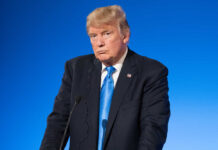 Man in suit with blue background speaking at podium.