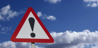Warning sign with exclamation mark and blue sky background.