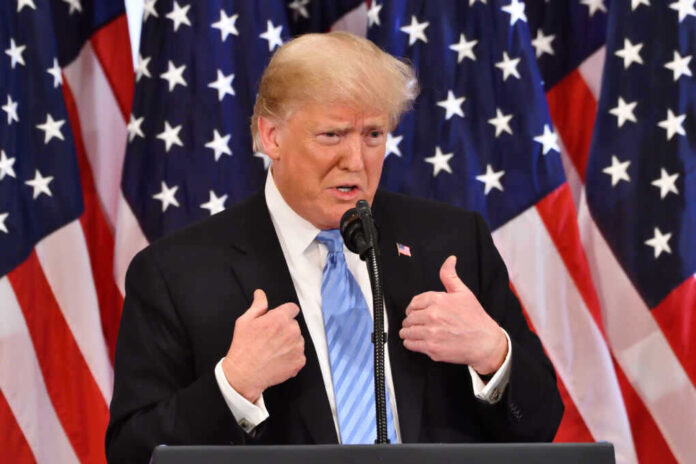 shutterstock_1200585187.jpg featured image Donald Trump speaking in front of multiple American flags.