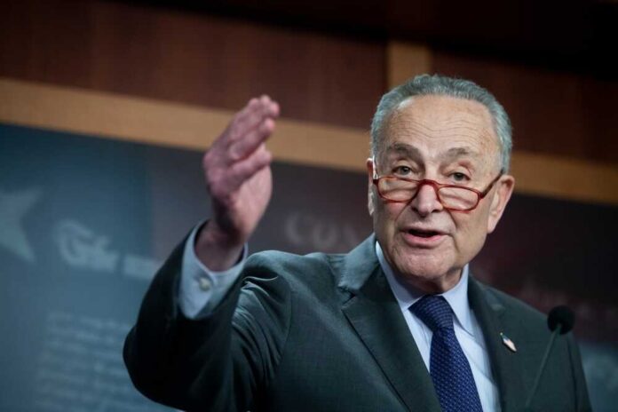 shutterstock_2274415101.jpg featured image Chuck Schumer gesturing while speaking at a podium indoors.