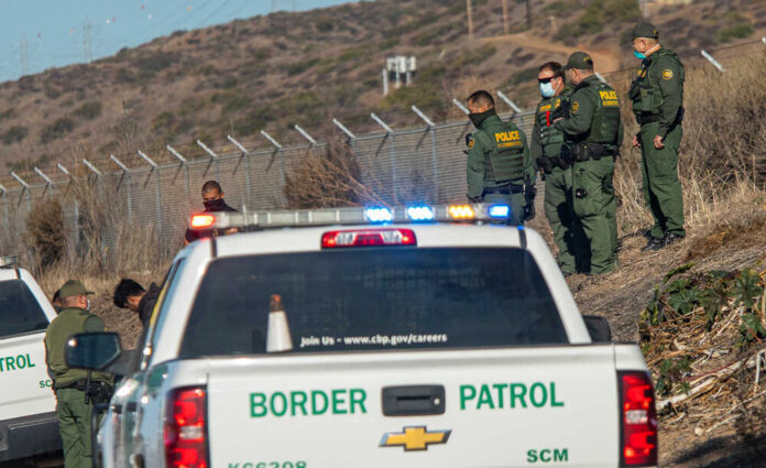 shutterstock_19008684462.jpg featured image Border Patrol officers detaining individuals near a fence.