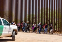 Group of people walking by a border fence.