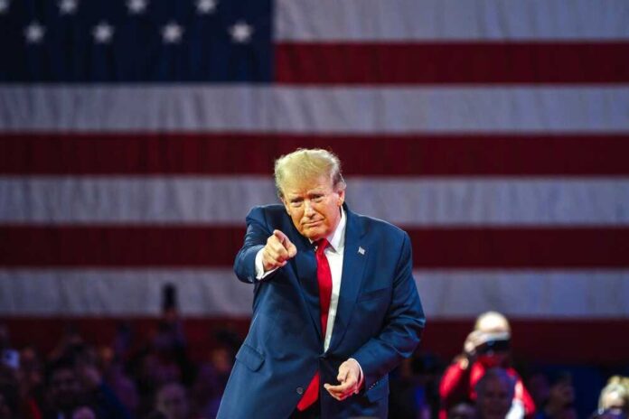shutterstock_2455396913-1.jpg featured image Donald Trump in front of American flag pointing toward camera.