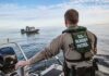Border Patrol officer on boat watching another boat.
