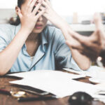 Stressed woman with hands on face at a desk.