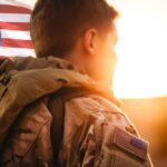 Soldier in uniform with American flag at sunset.