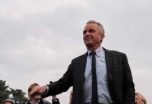 Robert F. Kennedy Jr. in a suit stands outdoors, cloudy sky background.