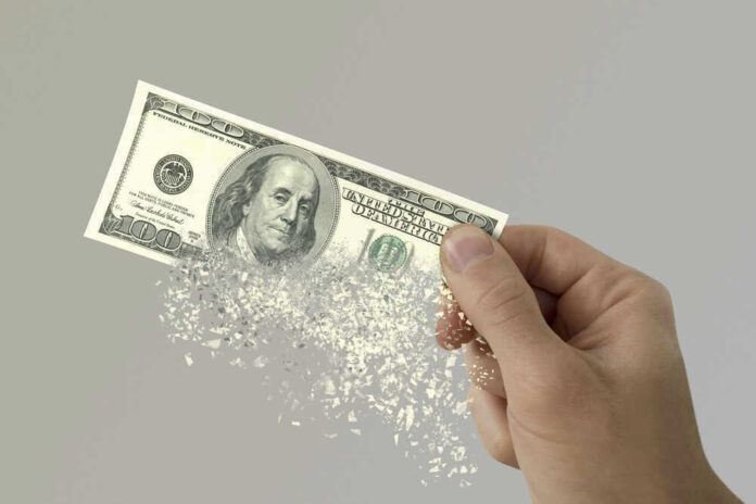 Hand holding a disintegrating hundred dollar bill.