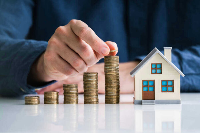 Hand stacking coins beside a miniature house model.