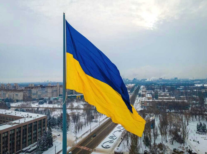 Ukrainian flag flying over snow-covered city landscape.