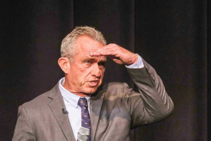 Robert F Kennedy in gray suit shielding eyes.