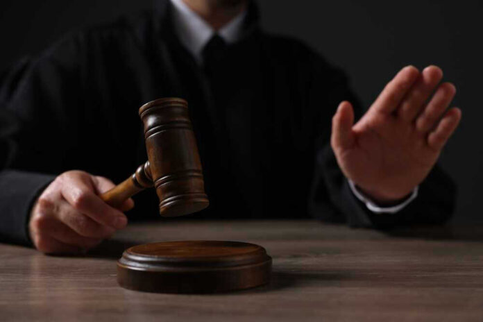 Judge holding gavel, hand raised in courtroom.