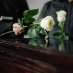 Two individuals placing white roses on a coffin during a funeral