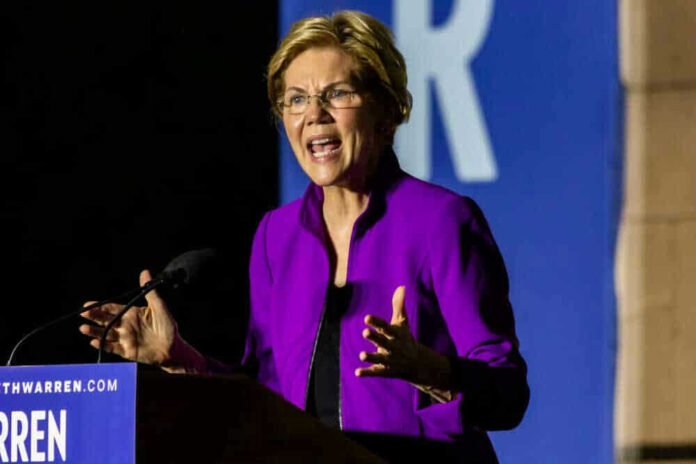 Elizabeth Warren speaking at podium wearing purple jacket.