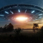 Large UFO hovering over a field at sunset.
