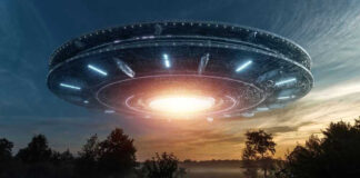 Large UFO hovering over a field at sunset.