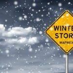 A yellow warning sign indicating a winter storm amidst falling snow
