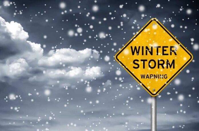 A yellow warning sign indicating a winter storm amidst falling snow