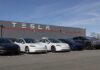 A lineup of Tesla cars parked in front of a Tesla building