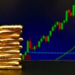 Stack of gold bars in front of a stock market chart
