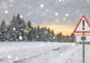 Snow-covered road with a warning sign and pine trees in the background