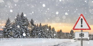 Snow-covered road with a warning sign and pine trees in the background