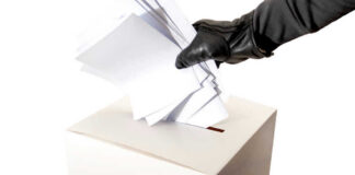 Gloved hand placing multiple papers in a ballot box.