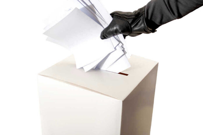 Gloved hand placing multiple papers in a ballot box.