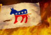 Torn Democratic flag burning amid flames and embers.