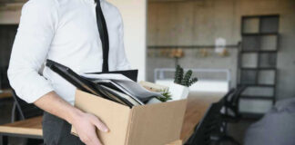 Person carrying box of office supplies in workspace.
