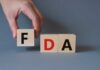 A hand holding a wooden block with the letter F, next to blocks spelling FDA