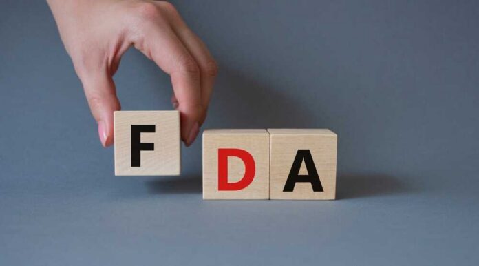A hand holding a wooden block with the letter F, next to blocks spelling FDA