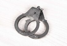 A pair of metallic handcuffs resting on a light wooden surface