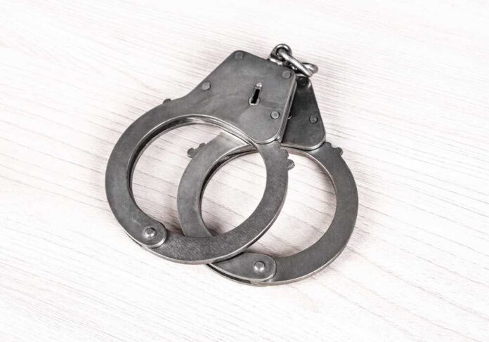 A pair of metallic handcuffs resting on a light wooden surface