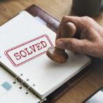 A hand applying a stamp marked 'SOLVED' on a notebook