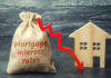 A burlap sack labeled Mortgage interest rates next to a wooden house and a downward red arrow
