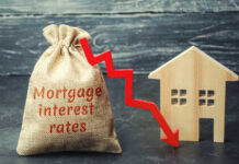 A burlap sack labeled Mortgage interest rates next to a wooden house and a downward red arrow