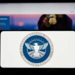 A hand holding a smartphone displaying the Transportation Security Administration logo