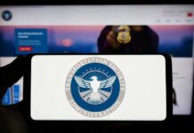 A hand holding a smartphone displaying the Transportation Security Administration logo