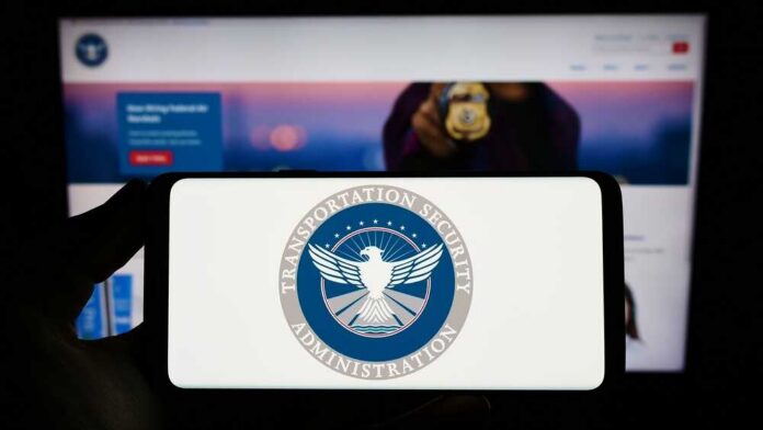A hand holding a smartphone displaying the Transportation Security Administration logo