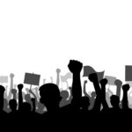 Silhouetted crowd of protesters raising fists and holding signs