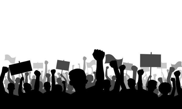 Silhouetted crowd of protesters raising fists and holding signs