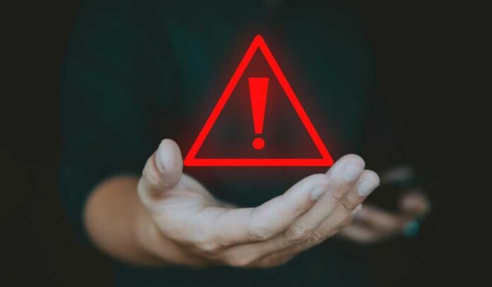 shutterstock_2420383835.jpg A hand holding a red warning triangle with an exclamation mark