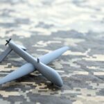 A gray drone model placed on a camouflage patterned surface