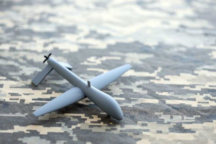 A gray drone model placed on a camouflage patterned surface